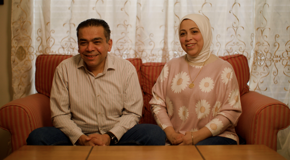 A smiling married couple sits on a sofa in the new home they purchased with the help of funding from an FHLBank Boston homebuyer assistance program.