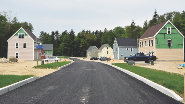 partially built homes  lining a paved road with a pick-up truck and cars parked in front of one of the homes