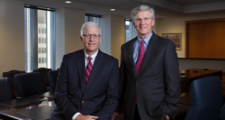 FHLBank Boston president sitting on a board room table with his hands folded on his lap with the current FHLBank Boston president standing beside him.