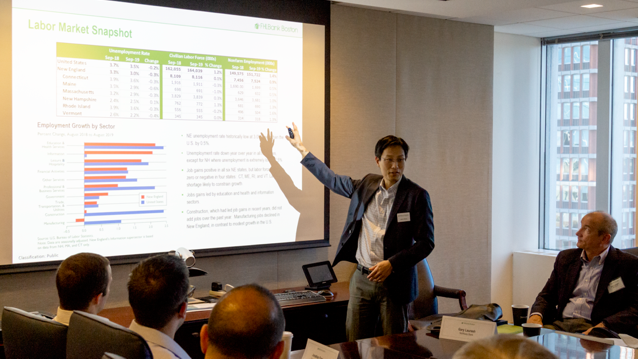 man pointing to a screen and speaking to an audience of seated people