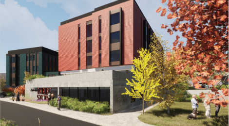 brick apartment building surrounded by trees and greenery and people walking along a sidewalk out front, while other stand on grass by trees next to building