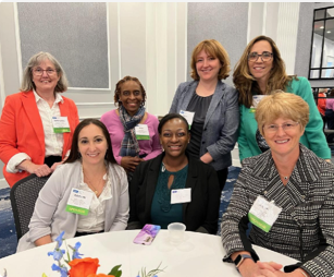 Group of seven female FHLBank Boston employees with four standing next to each other behind three that are seated at a round table.