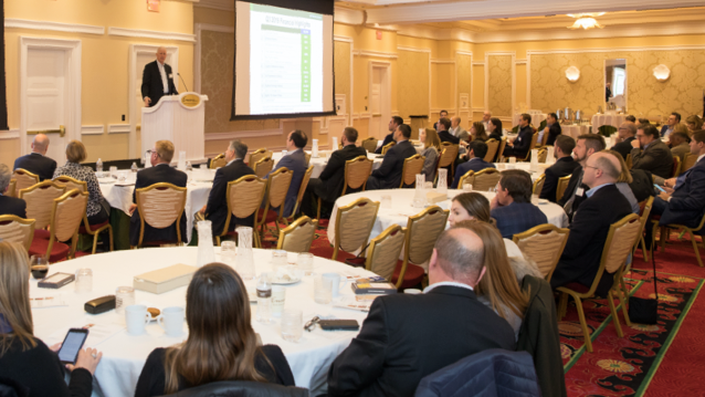 FHLBank Boston president standing at the podium addressing audience members seated at round tables