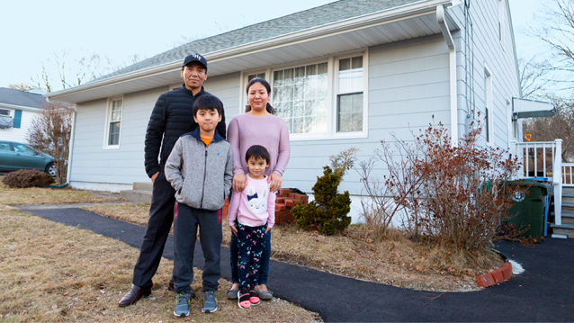 father, mother, and son and daughter outside with home in background