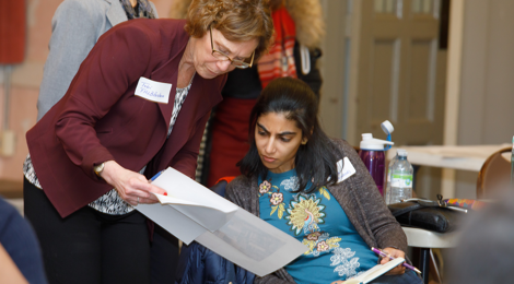 woman standing next to seated woman as they both review a document