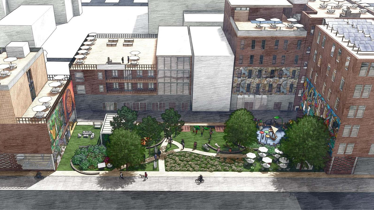 Overhead shot of a series of multi-level buildings with a greenspace with trees, walkways, a playground, and people walking in the middle