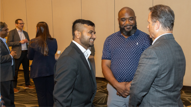 Three men standing next to each other in a hotel conference room as they chat