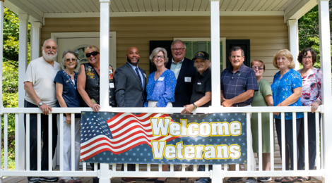 a mix of five men and six women standing next to each other on a porch with a welcome veterans banner draped over the porch railing