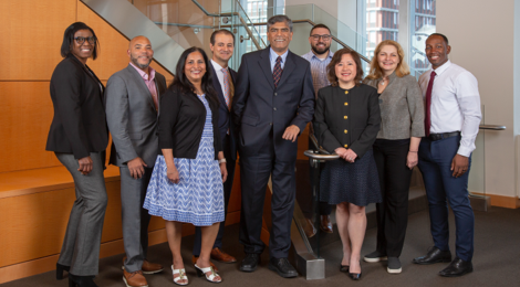 Mix of nine women and men who make up the Inclusion Council smiling and standing in front of a staircase in an office lobby