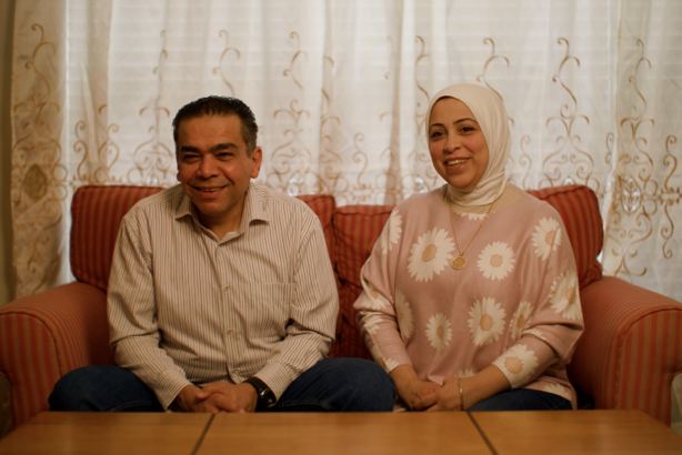 A smiling man and woman sitting next to each other on a couch in their living room.