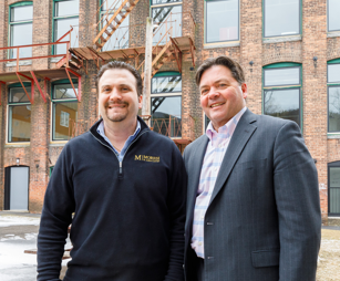 two men standing in front of an old mill building that was redeveloped
