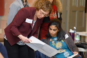 female senior community investment manager standing as she reviews a document with a female student coordinator who is seated
