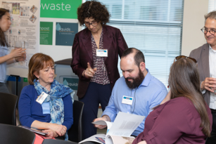 woman standing over seated woman and man who are reviewing documents
