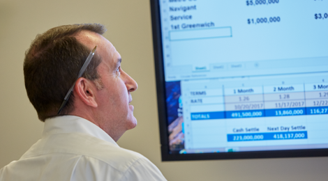 man with a pen behind his ear standing and reviewing data on a large screen before him