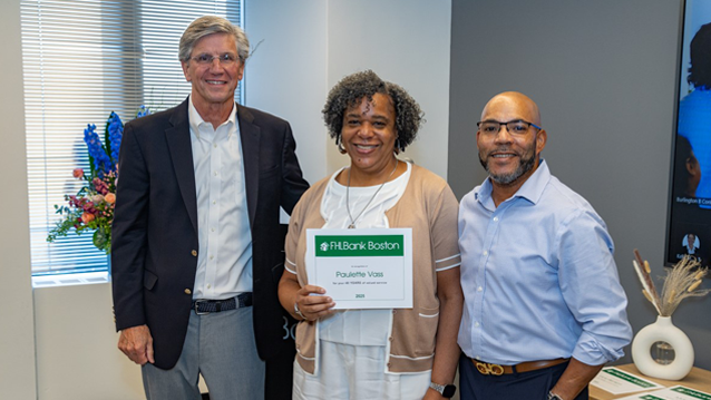 Smiling woman holding a certificate in front of her while standing between two men.