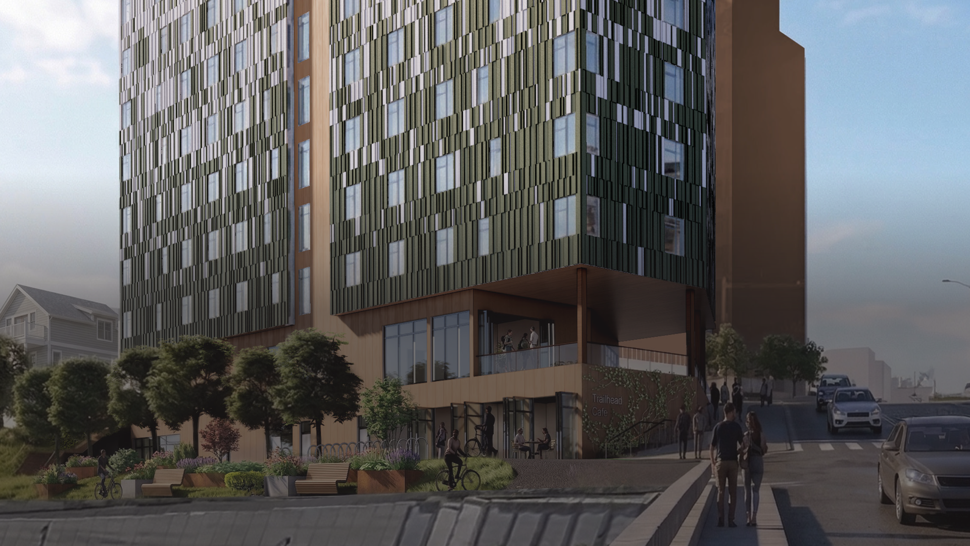 multistory building with cyclist on a paved community path in front of it and pedestrians walking past next to a road with cars driving past
