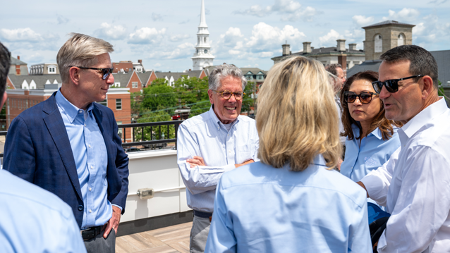 three men and two women chatting with each with a view of downtown Portsmouth in the background