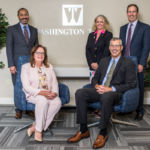 woman and man wearing professional attire in chairs with a woman and two men standing behind them and the Washington Trust logo in background