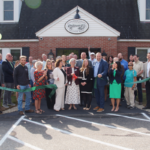 a large group of men an women standing outdoors in front of a Merrimack County Savings Bank cutting a large ribbon with balloons at each side