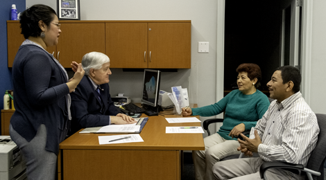 female standing near desk with man seated at desk and male and female couple seated in front of desk looking at seated male