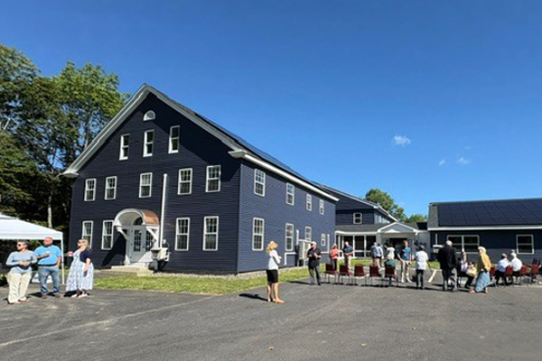 Exterior of an apartment complex with people and chairs along a paved area next to it.