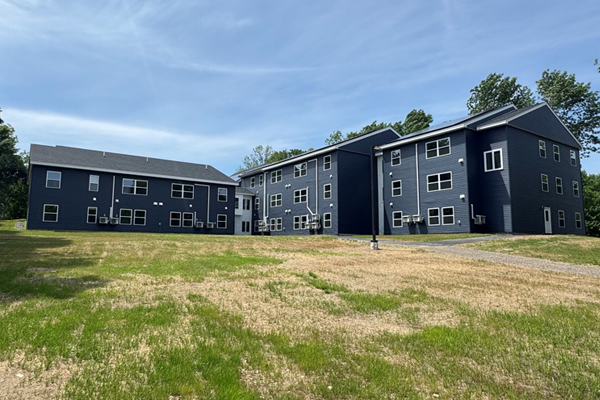 Exterior of the back of an apartment building with a wide grassy area before it.
